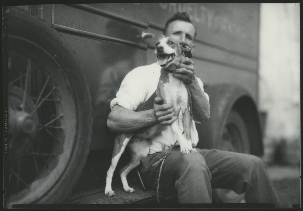 A man sitting on the back of a truck, holding a dog