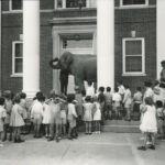 school students facing a building with an elephant behind two pillars